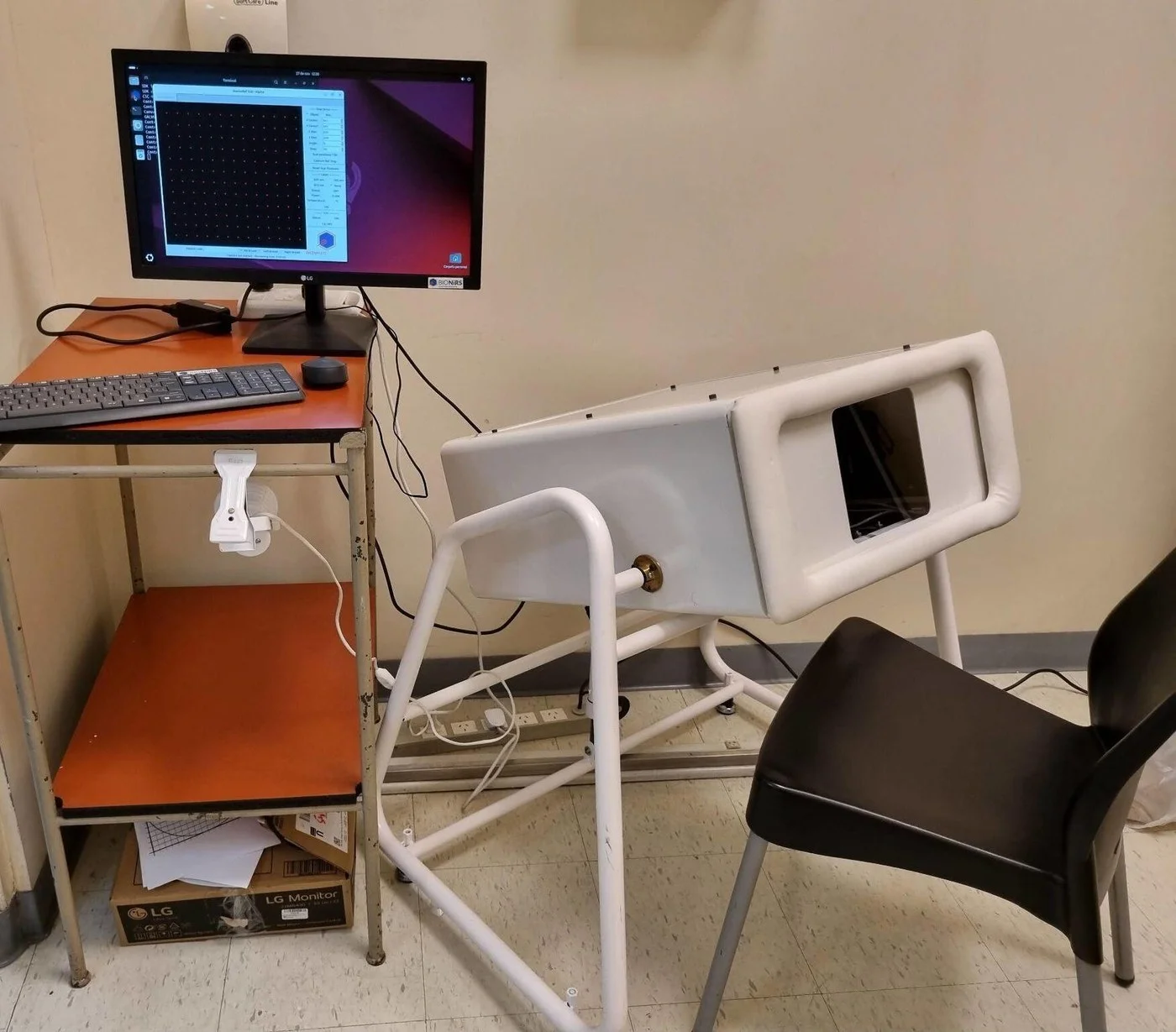 Prototipo V2 de MamoRef instalado en un consultorio hospitalario, junto a la computadora con el software de control y la silla de la paciente